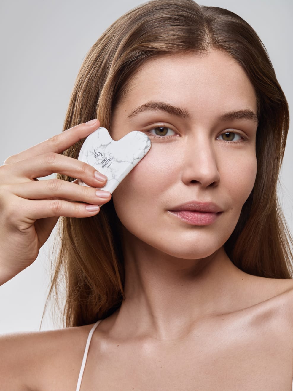 Model hält Gua Sha Stein an die Wange