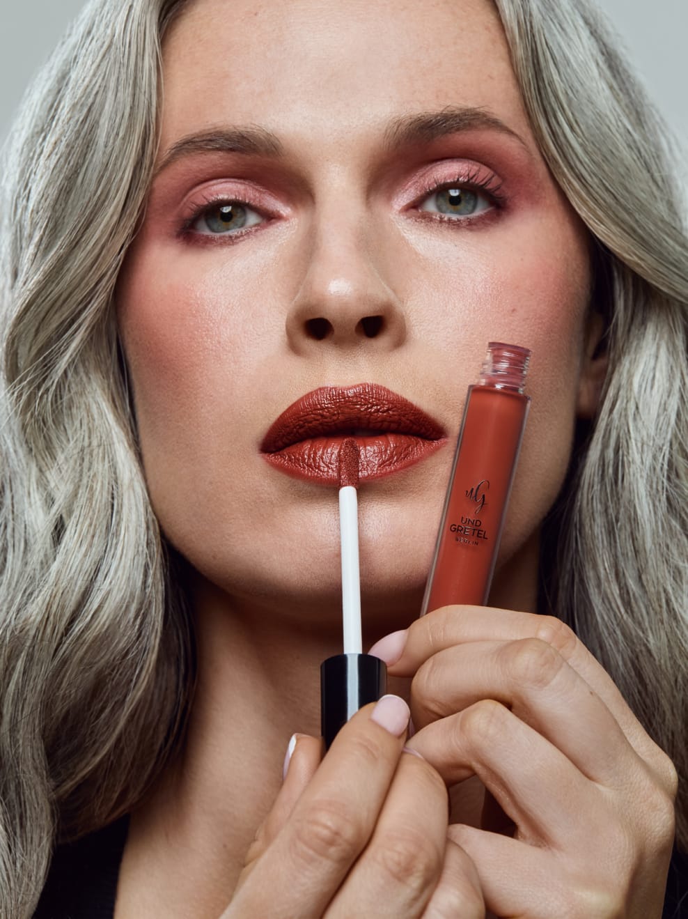 Model trägt Kus 04 auf und hält den Lipstick in der Hand