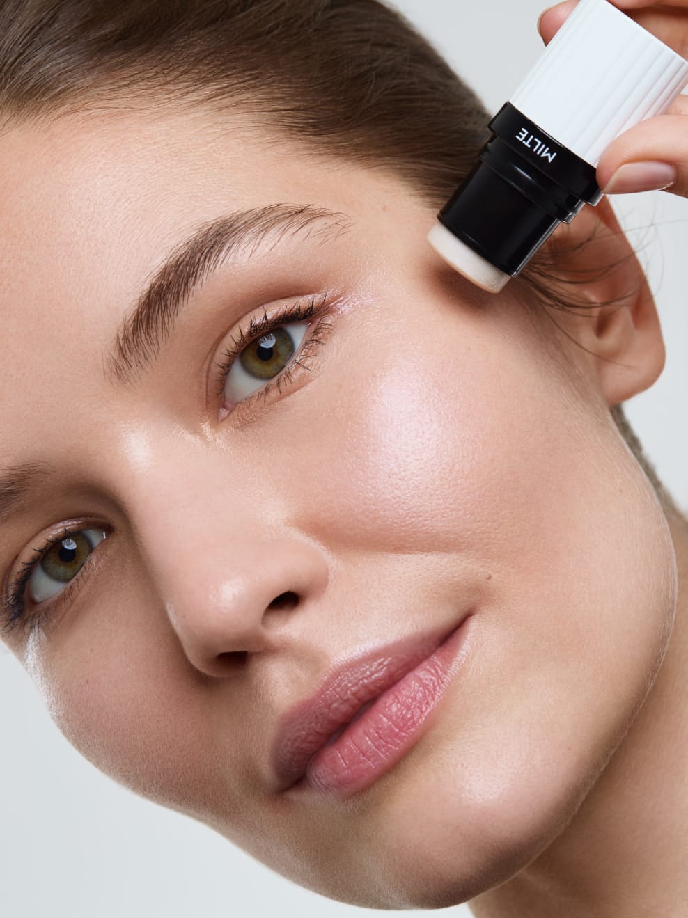 Model geschminkt Milte Highlighter und hält den Stick an die Wange