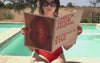 Frau mit rotem Badeanzug und Sommer Sale Zeitung am Pool